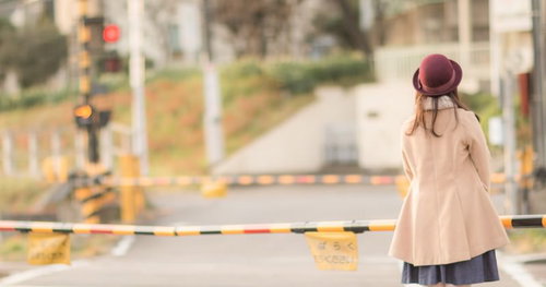 踏切で赤信号を待つスマートフォンを持つ女性