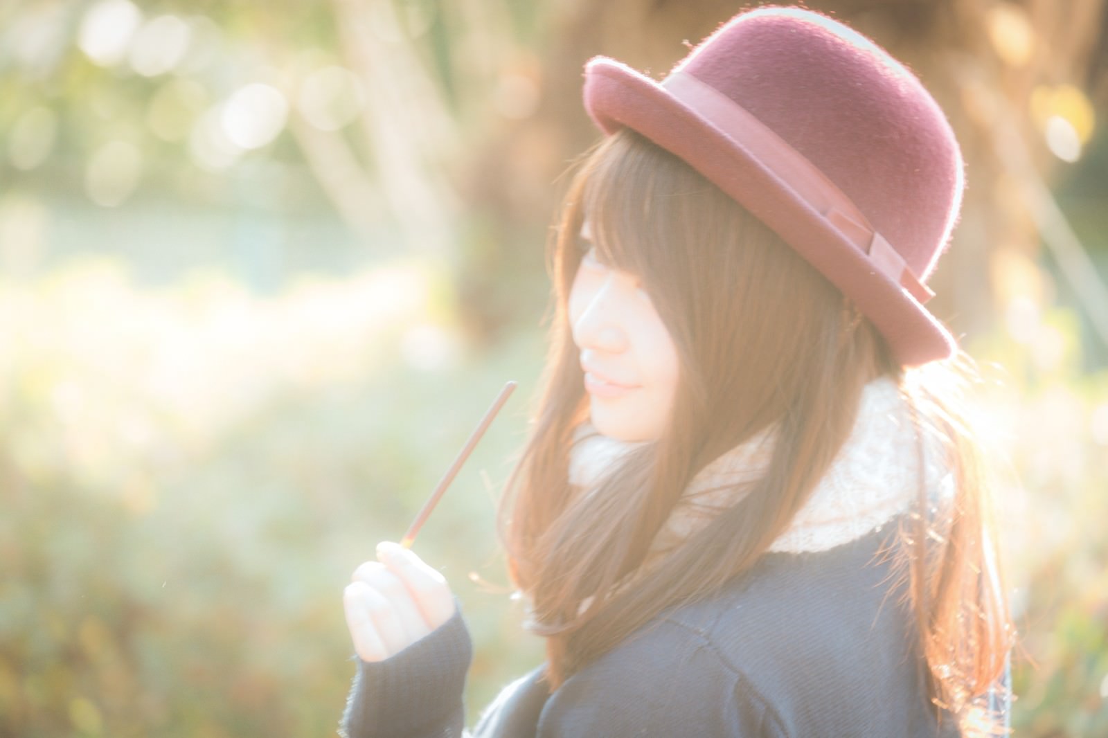 ピンク帽子をかぶってお菓子を持つ女性が屋外でおやつタイムを過ごしている写真［モデル：茜さや］