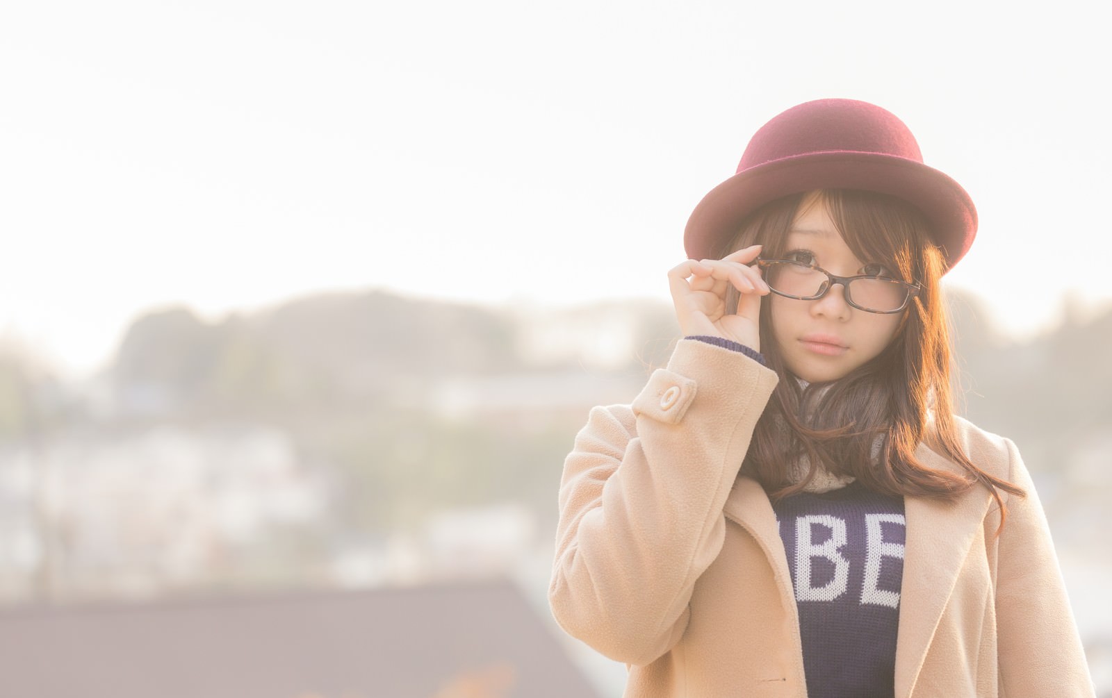 ベージュのコートとボルドー帽をかぶり、眼鏡をかけた女性が正面を向いている［モデル：茜さや］