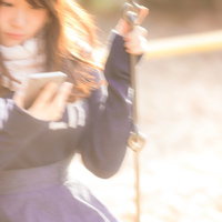 公園のブランコに揺られながらスマホを操作する女性の写真