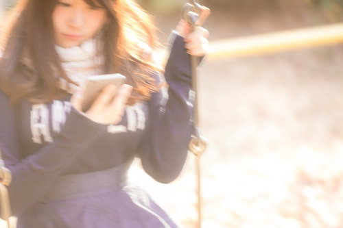 公園のブランコに揺られながらスマホを操作する女性