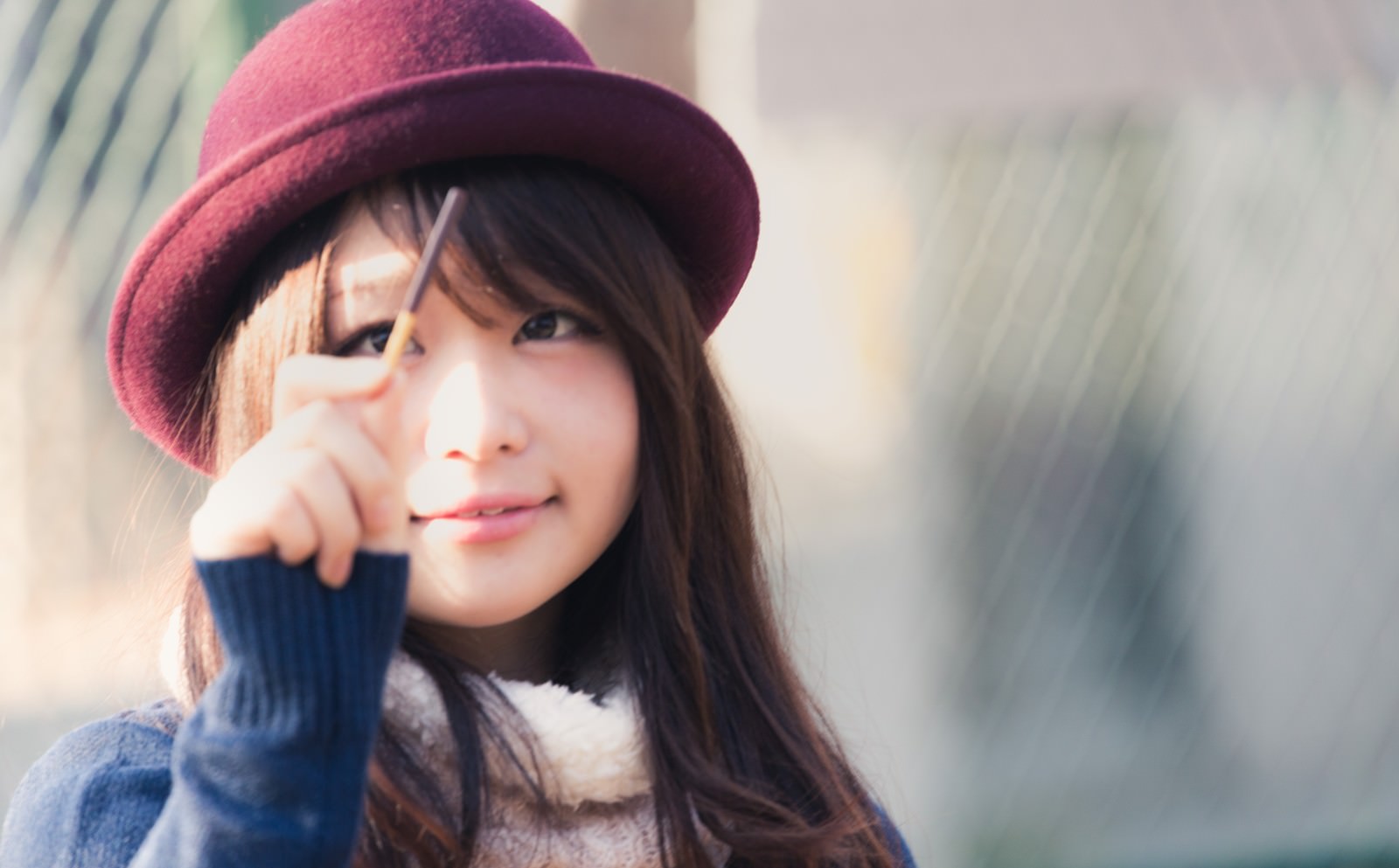 赤紫のベレー帽をかぶった女性がポッキーを持ち、頬に手を当てて笑顔で上目遣いしている［モデル：茜さや］