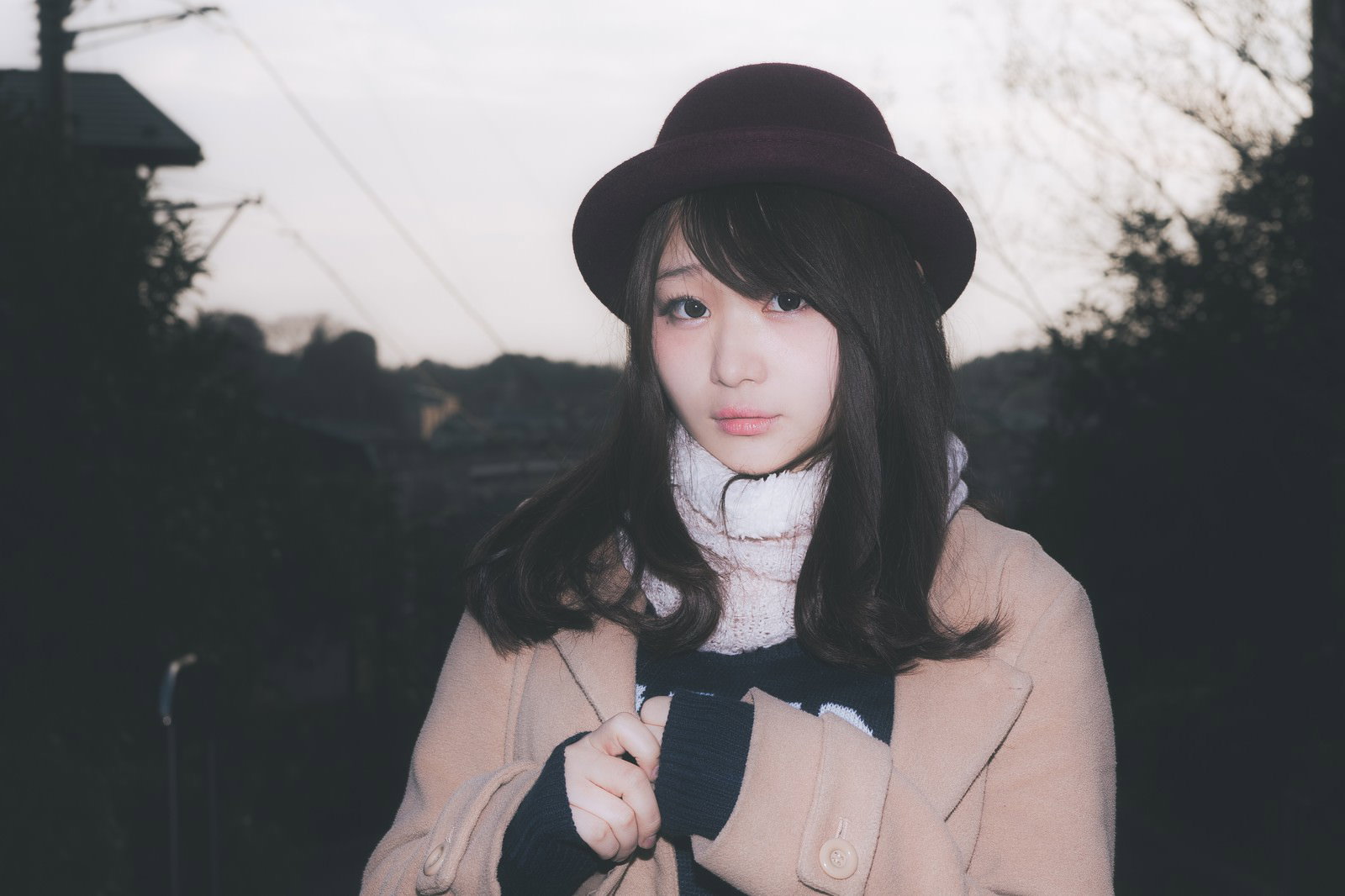 夕暮れ時に不安そうな表情で上を見つめるコート姿の女性［モデル：茜さや］
