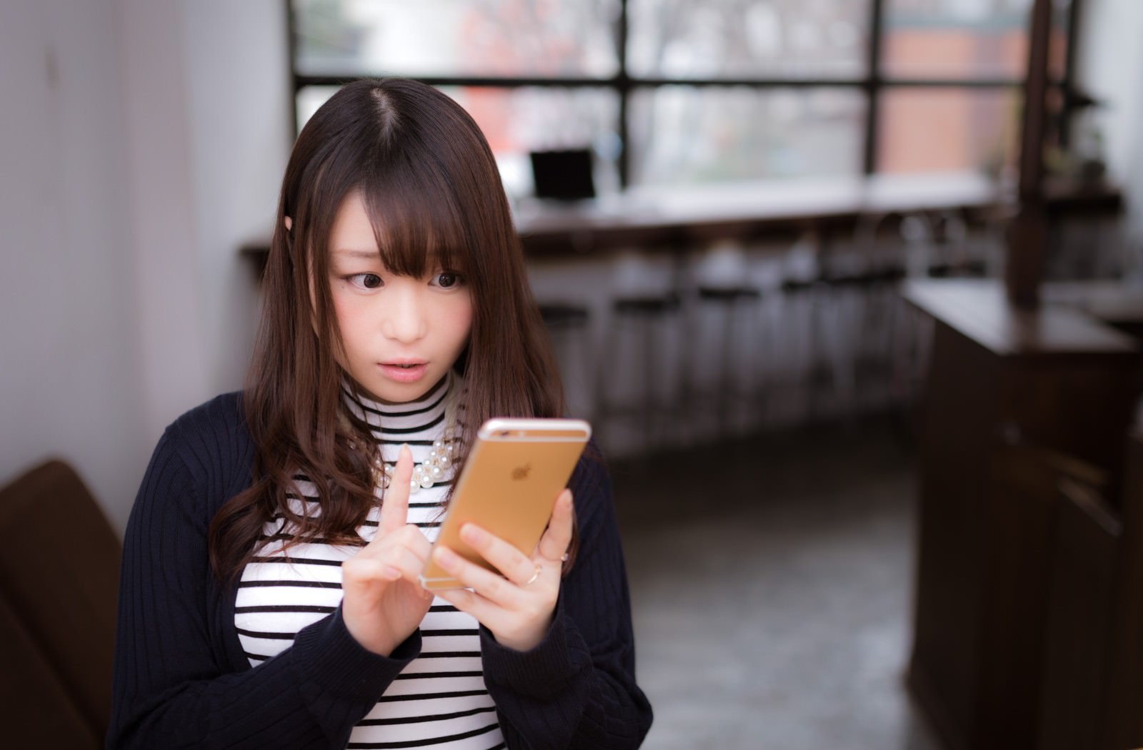 カフェでスマートフォンを見ながら驚く女性［モデル：茜さや］