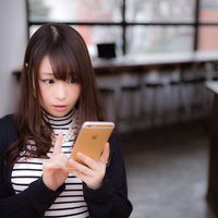 カフェでスマホを見て驚く表情のOL女性、反応を示す姿の写真