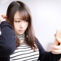 スマホを鏡代わりにしてヘアメイクをチェックする女性の写真