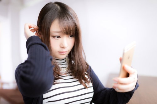 スマホを鏡代わりにしてヘアメイクをチェックする女性