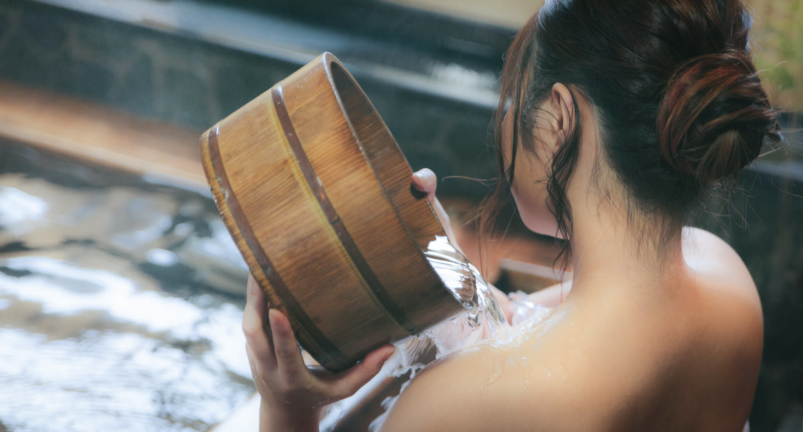 檜風呂で桶を使って肩にかけ湯する女性の後ろ姿［モデル：茜さや］
