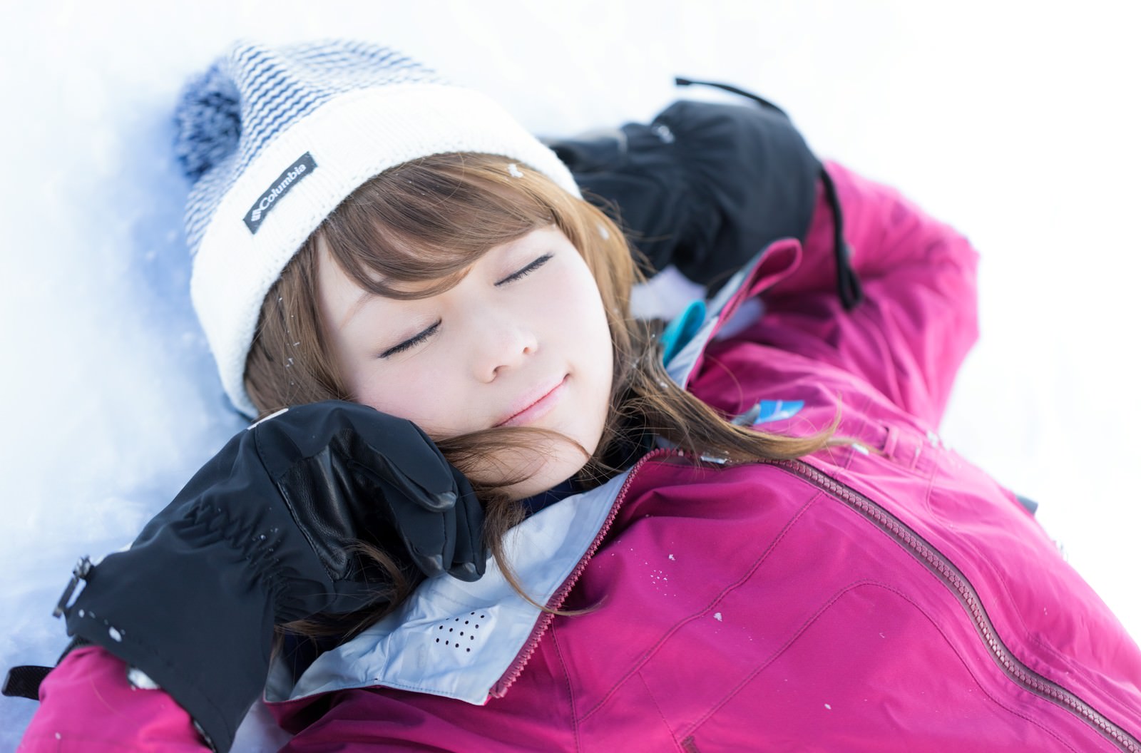 雪の上に仰向けに寝転ぶスキーウェア姿の女性［モデル：茜さや］