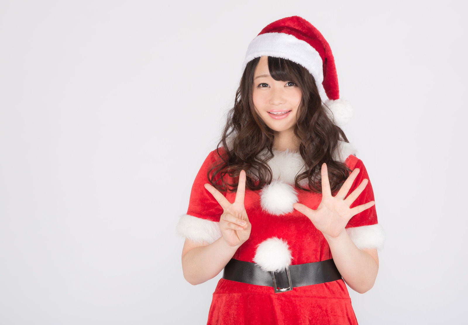 赤いサンタ衣装を着た女性が両手でピースサインをして笑顔で正面を向いている［モデル：茜さや］