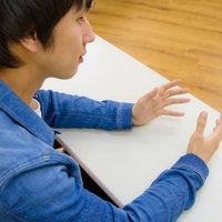 デスクに座ってろくろを回すような手つきの男性の写真