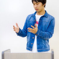 登壇してろくろを回すような手つきの男性の写真