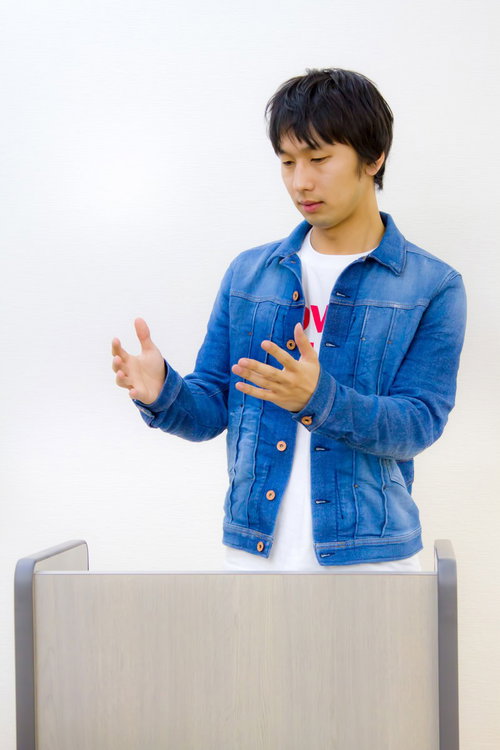 登壇してろくろを回すような手つきの男性