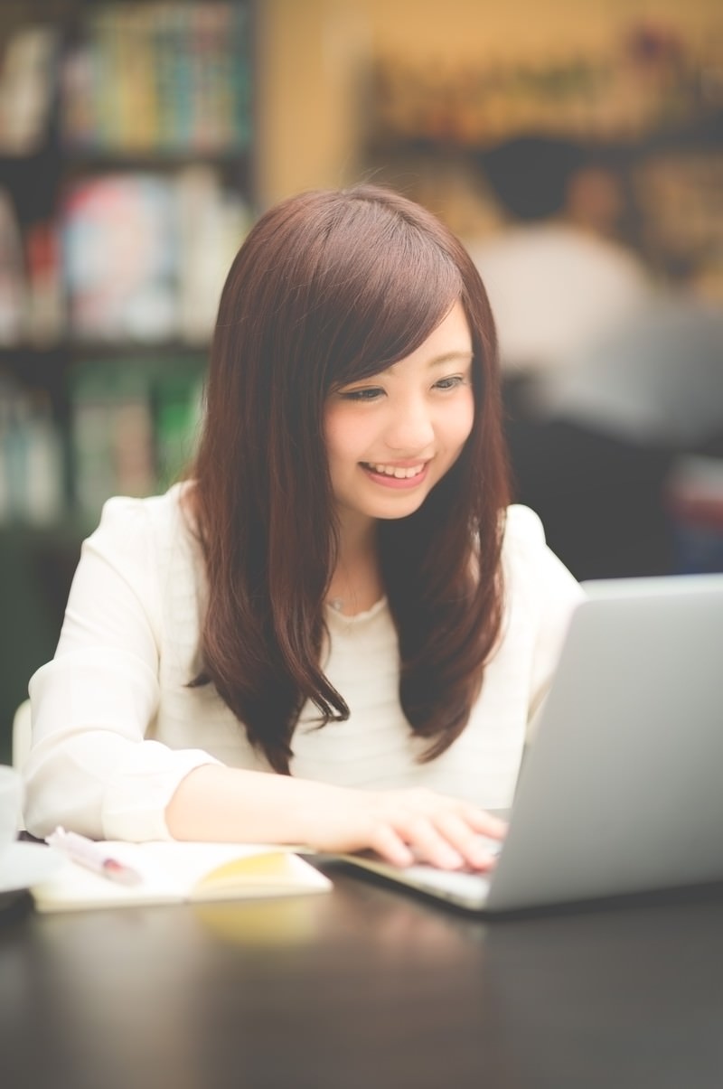 カフェでノートパソコンを操作して作業する白いシャツの女性［モデル：河村友歌］