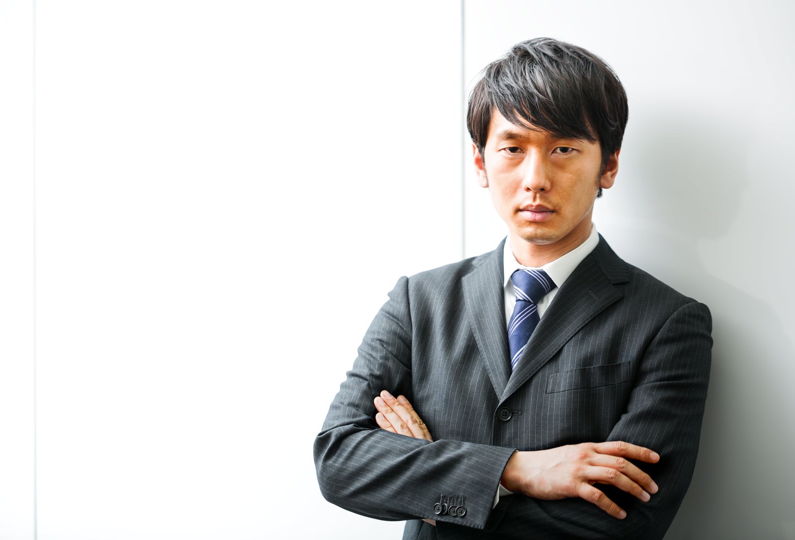 腕を組んで正面を見つめるスーツ姿の日焼けした男性［モデル：大川竜弥］
