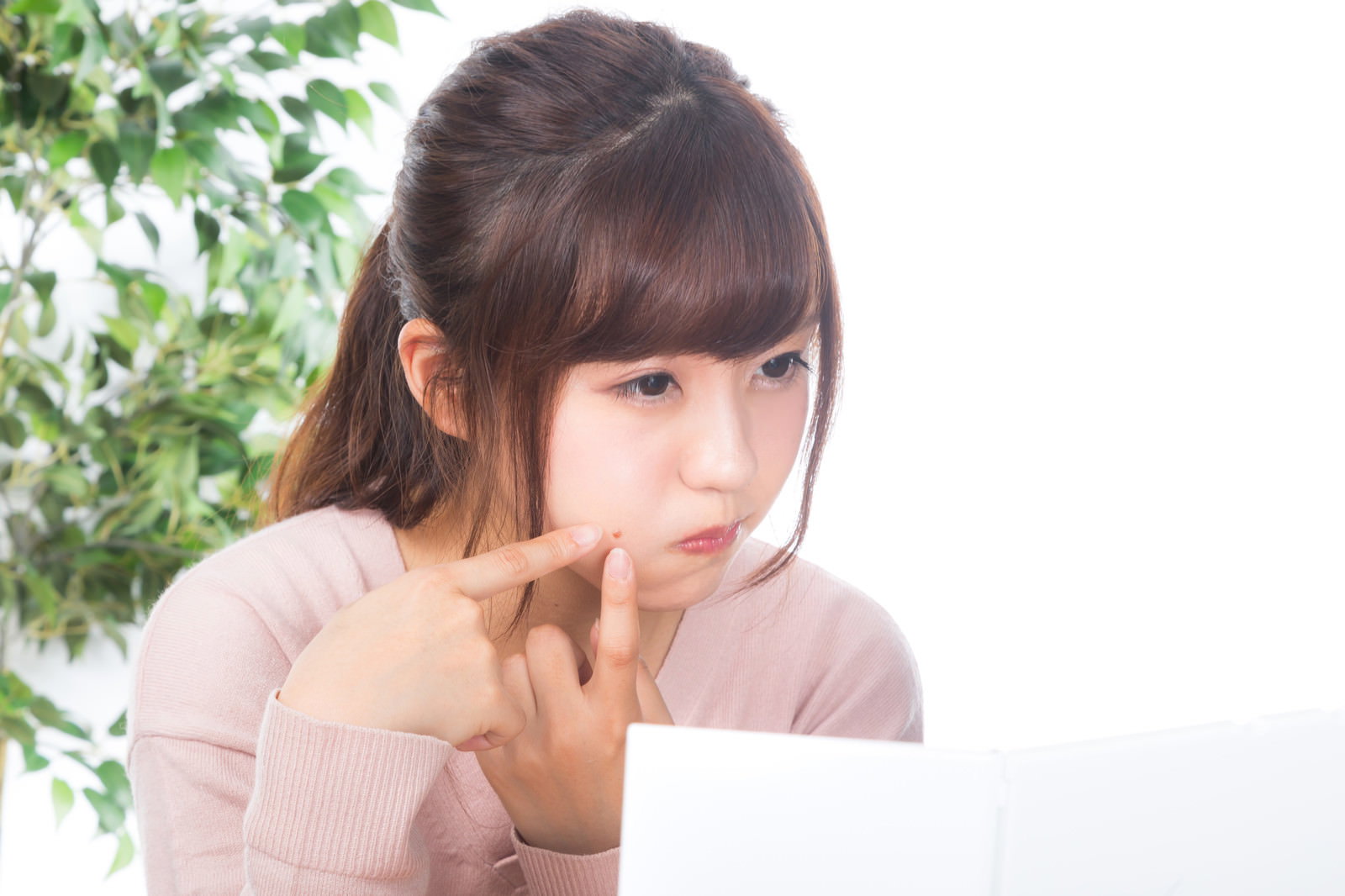 鏡を見ながら頬のニキビを気にする若い女性［モデル：河村友歌］