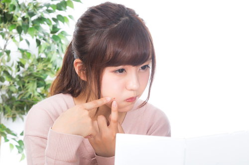 鏡を見ながら頬のニキビが気になる若い女性