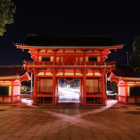門から見えるヘッドライトの光跡と夜景の神社の写真