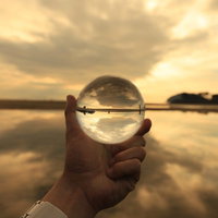 手に持った水晶球に映る夕焼けの砂浜風景の写真