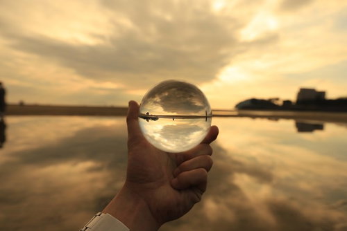 手に持った水晶球に映る夕焼けの砂浜風景