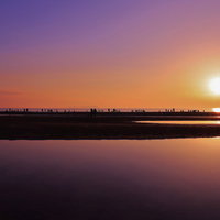 沈む夕日と浜辺で遊ぶ人々のシルエット、海面リフレクションの写真
