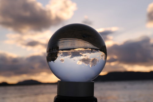 ガラス玉に映る朝焼けの海岸と雲の風景、透明な水晶球の光の反射