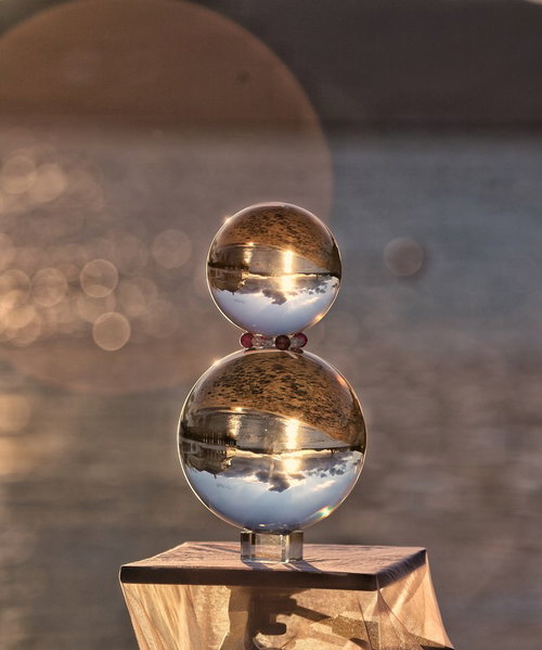 木製の台に重ねたガラス玉と湖面に煌く夕日の玉ボケ