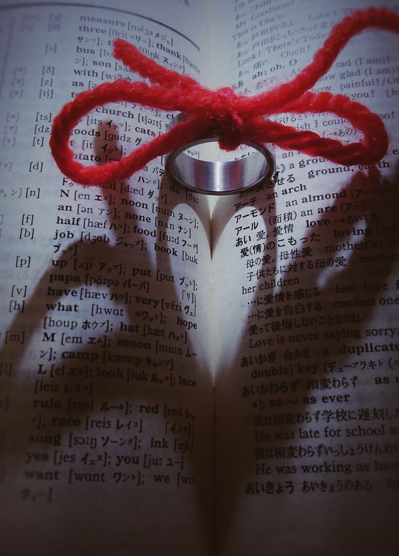 辞書のページから浮かび上がるハート形と赤い糸で結ばれた指輪