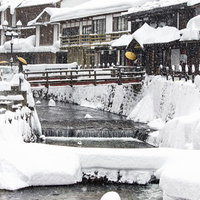 雪が降る銀山温泉の川沿いの木造建築の写真