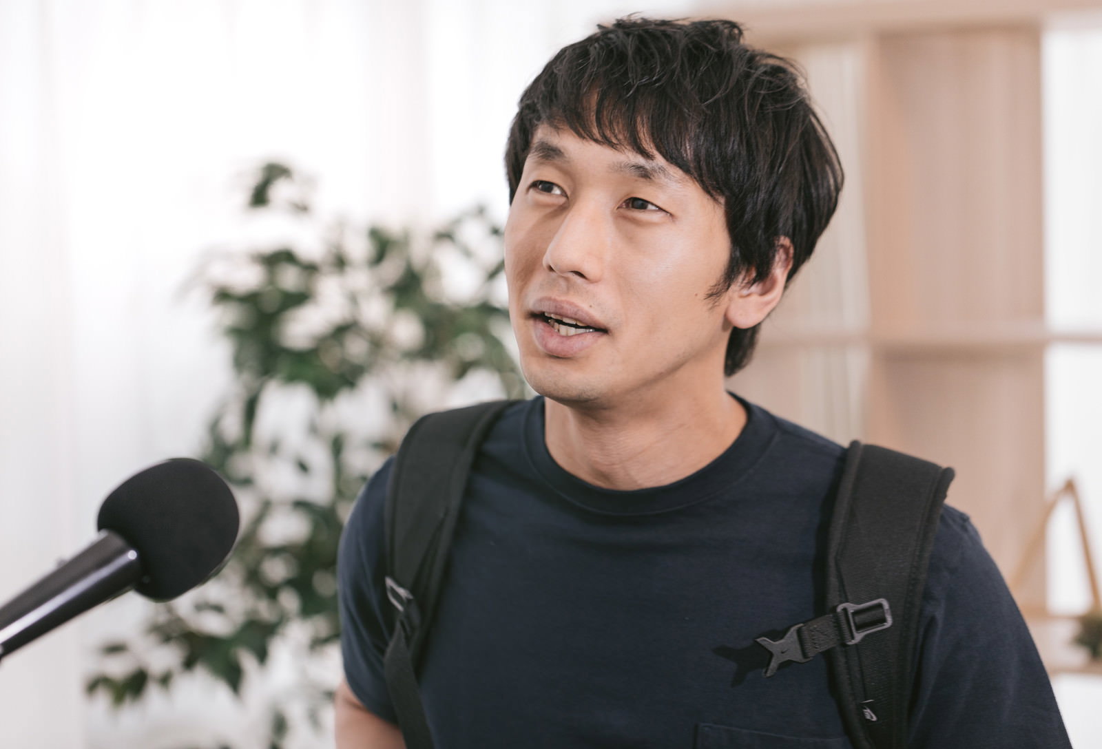 マイクの前でインタビューを受ける黒いTシャツを着た男性