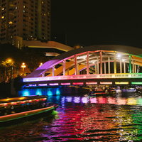 虹色にライトアップされたシンガポールの橋と屋形船の写真