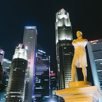 ラッフルズ像とライトアップされたビル群の夜景の写真