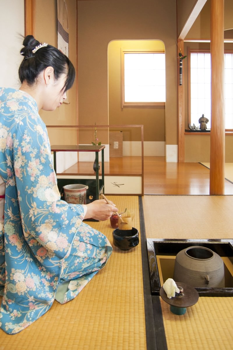 着物姿で畳の上に正座し茶碗に茶筅を入れてお茶を点てる女性