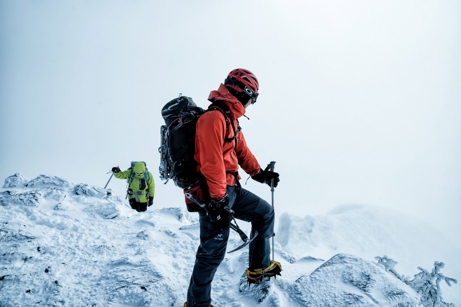 雪山の斜面で赤いジャケットを着て下山路を見つめる登山者の男性