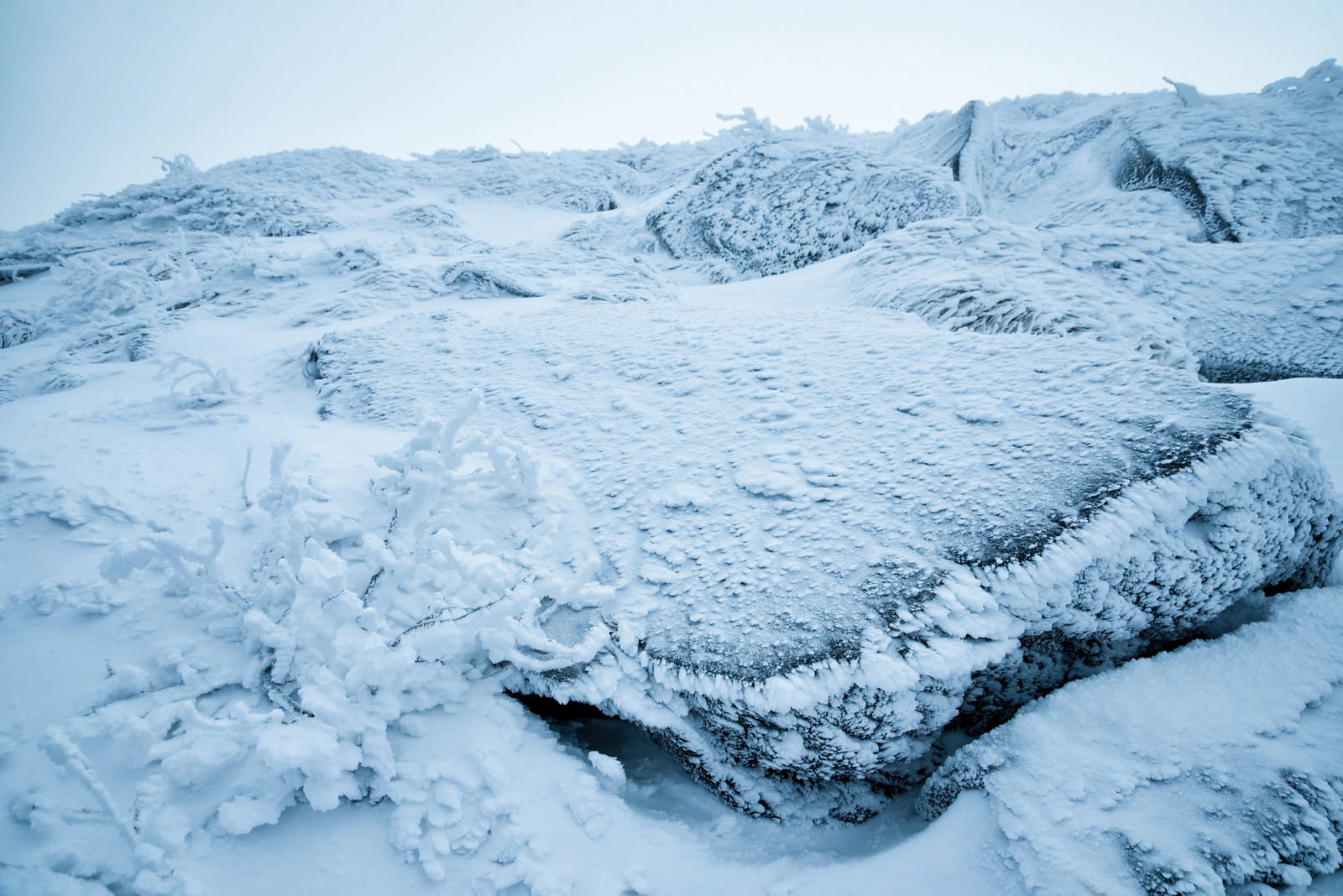 雪と氷に覆われた岩肌に小さな樹氷が付着している冬の風景