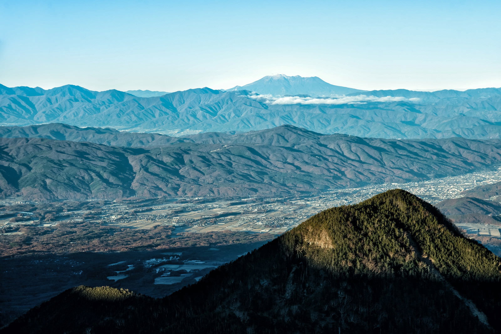 麓の町並みの向こうに雲に包まれた御嶽山が見える山岳風景