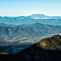 麓の町並みと遥か遠くの雲に包まれた御嶽山の写真