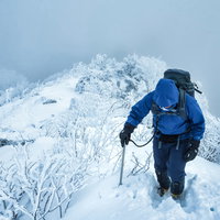 雪化粧した雪山の雪深い登山道で山頂を目指す登山者の写真