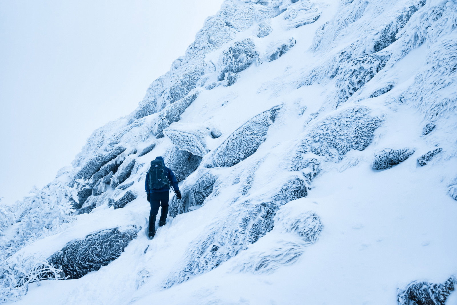 深い積雪に覆われた急峻な雪の斜面をトラバースする登山者