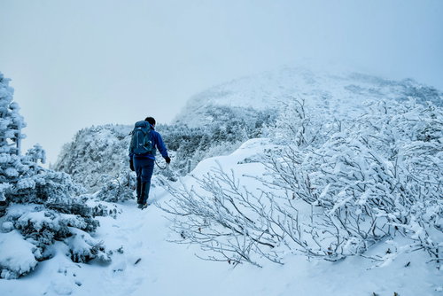 立ち込めたガスで隠れる山頂を目指す積雪の登山者