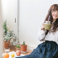 グリーンスムージーをおいしそうに飲む眼鏡の女性の写真