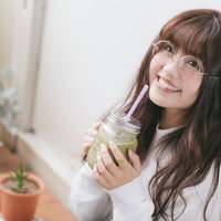 グリーンスムージーを飲んでリラックスする眼鏡の女性の写真