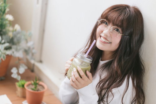 グリーンスムージーを飲んでリラックスする眼鏡の女性