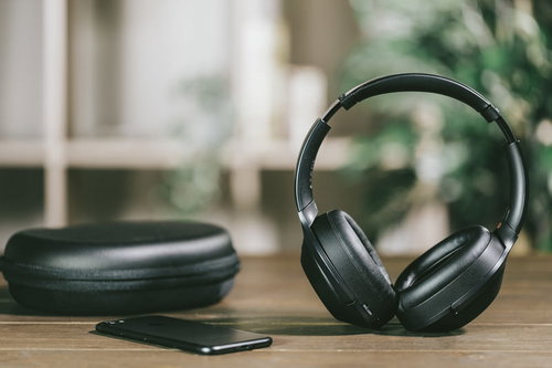 木製デスクに置かれたワイヤレスヘッドフォンとスマートフォン