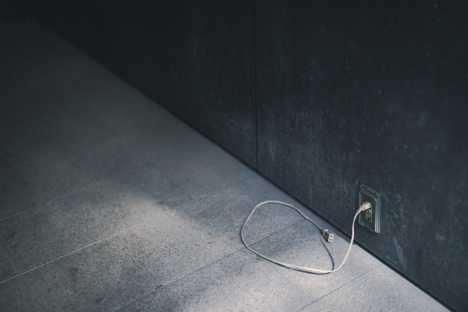 コンクリートの床に置かれた古びた白い電源コンセントと黒い延長ケーブル