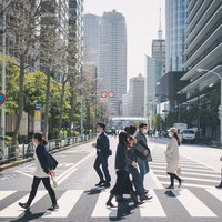 高層ビルが立ち並ぶオフィス街の横断歩道を渡る人たちの写真