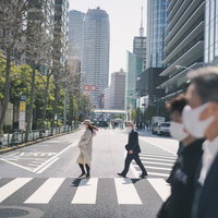マスク姿のビジネスマンが渡る横断歩道とオフィス街の写真