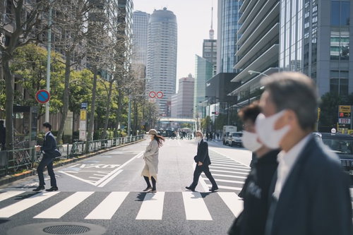 マスク姿のビジネスマンが渡る横断歩道とオフィス街
