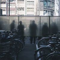 喫煙所にいる人のシルエットとガラス越しに見える奥の駐輪場の写真