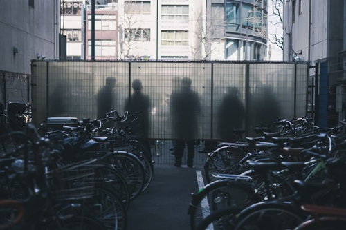 喫煙所にいる人のシルエットとガラス越しに見える奥の駐輪場